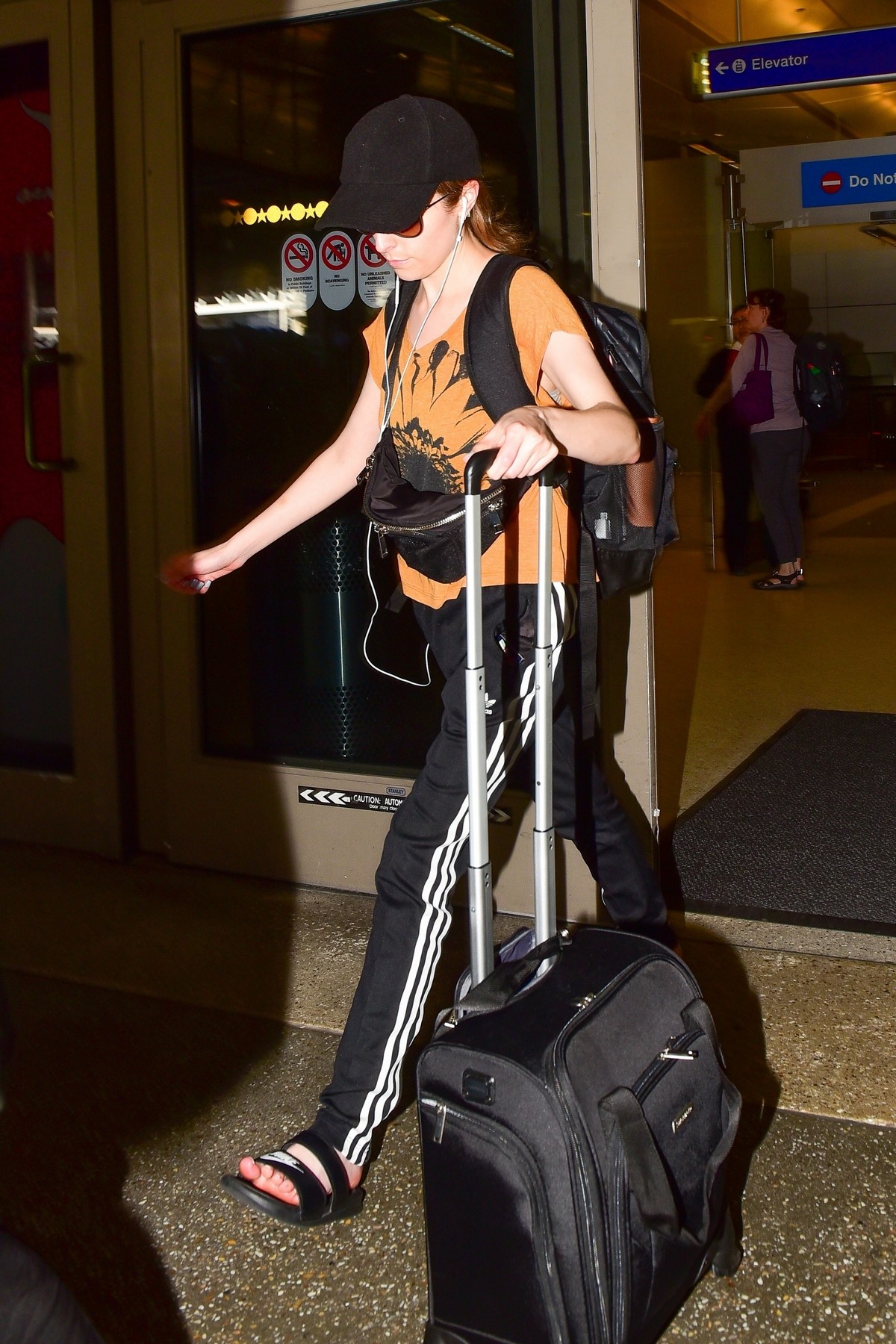 Anna Kendrick in Light Orange Top and Adidas Originals 3-Stripe Track Pants Out at LAX Airport in Los Angeles 2019/07/23