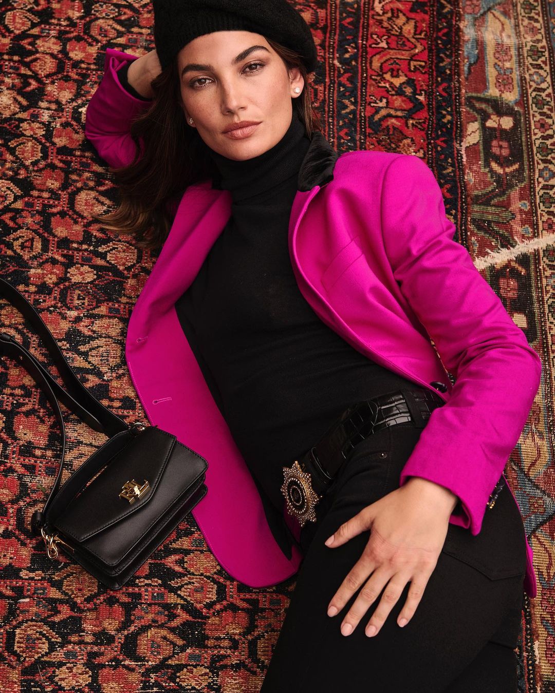 Portrait photoshoot of Lily Aldridge in a pink blazer and black beanie while lying on the carpeted floor beside a black purse