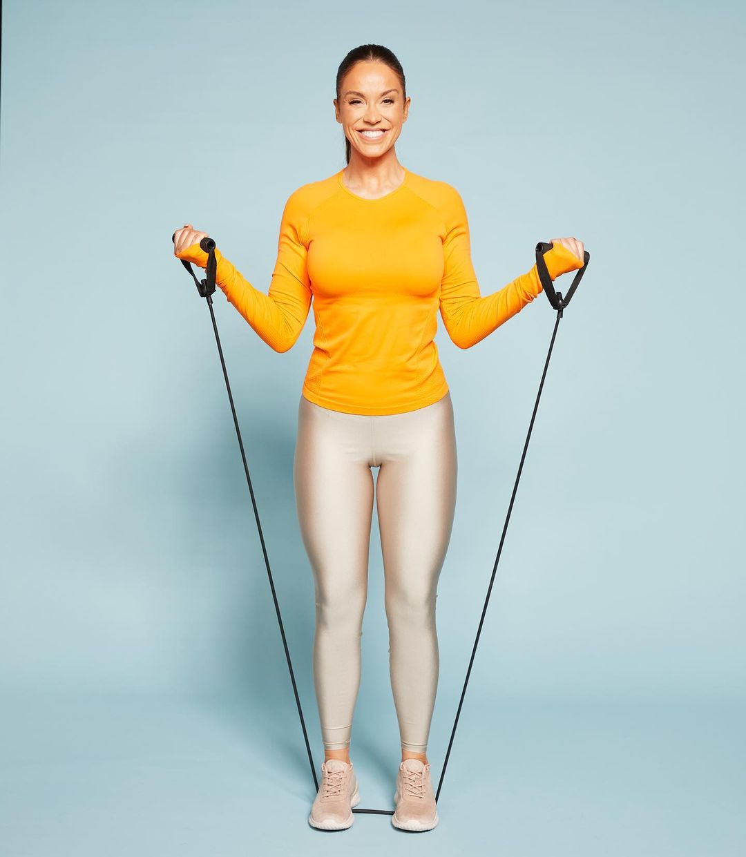 Television personality Vicky Pattison fitness photoshoot with resistance band for Fabulous Magazine wearing a orange t-shirt, silver leggings and skin color shoes