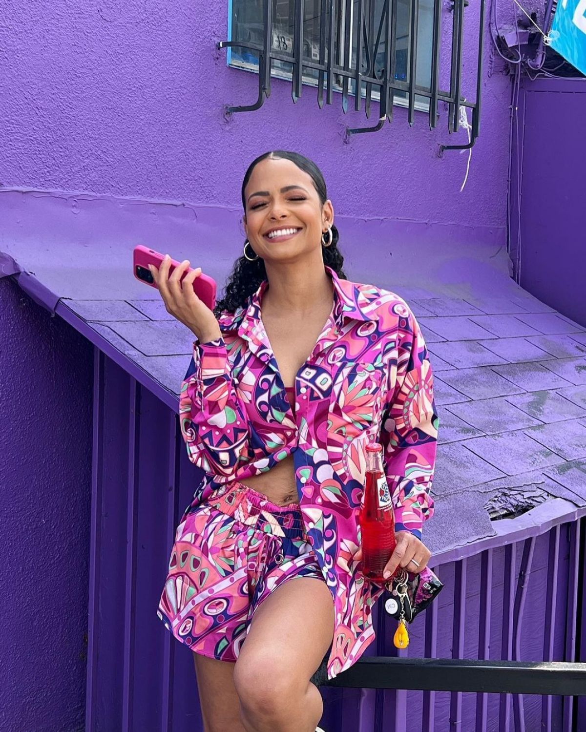 Christina Milian in a stylish floral dress against a purple wall