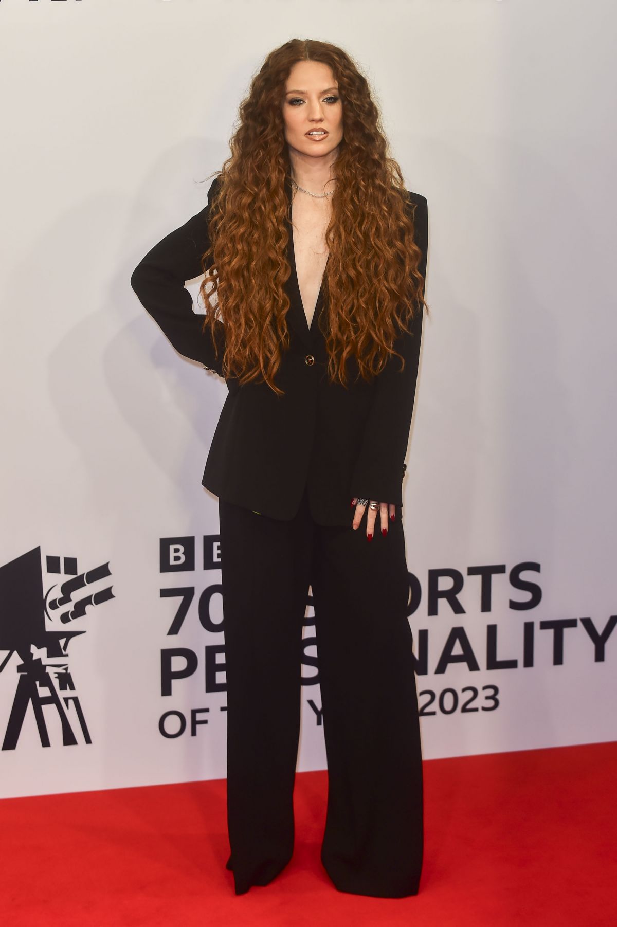 Person with long curly hair standing on a red carpet.