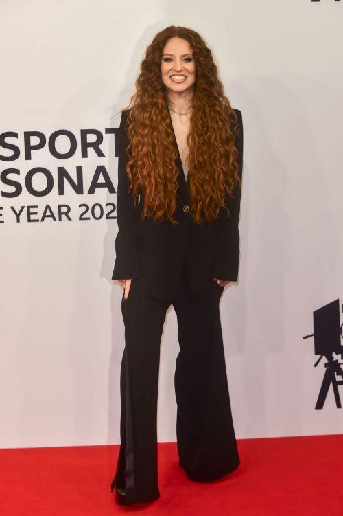 Person with long curly hair standing on a red carpet.