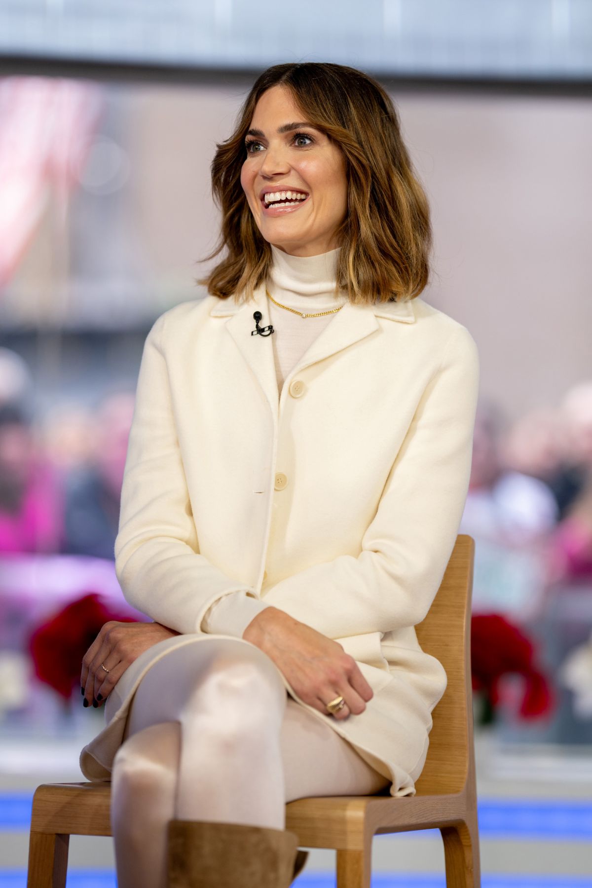 Mandy Moore sitting elegantly in white coat