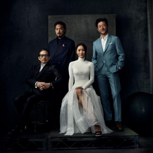 Anna Sawai posing with three other men, dressed in a white turtleneck and sheer skirt by Dior, in a formal group portrait setting.